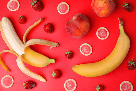 Flat lay composition with condoms and exotic fruits on red background. Erotic conceptの写真素材