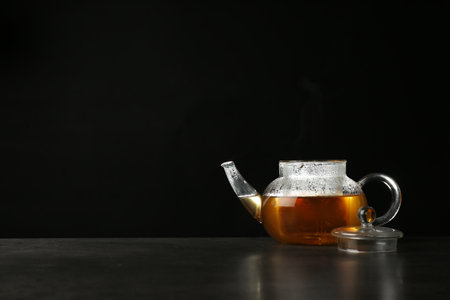Glass teapot with delicious hot beverage on table against dark background. Space for textの写真素材