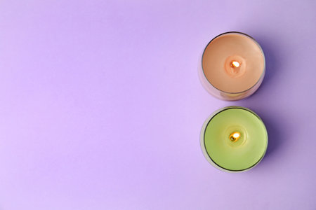 Burning wax candles in glass holders on purple background, flat lay. Space for textの写真素材