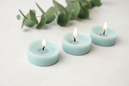 Burning light blue candles and eucalyptus branch on light tableの写真素材