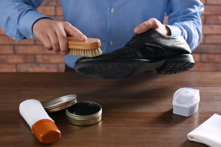 Man cleaning leather shoe at wooden table indoors, closeupの写真素材