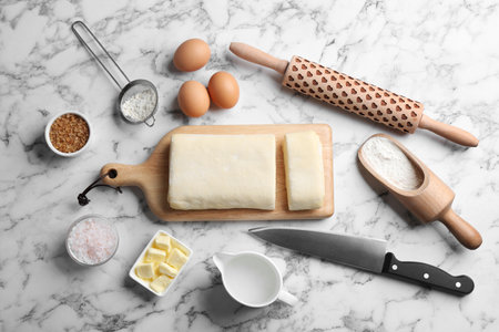 Flat lay composition of puff pastry dough and ingredients on white marble table