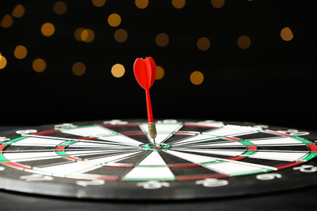 Red arrow hitting target on dart board against blurred lightsの写真素材