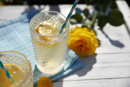 Glasses of refreshing lemonade and beautiful yellow rose on white wooden table. Space for textの写真素材