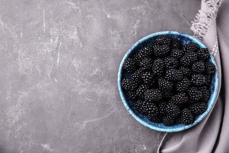 Bowl of ripe blackberries and fabric on gray table, flat lay with space for text