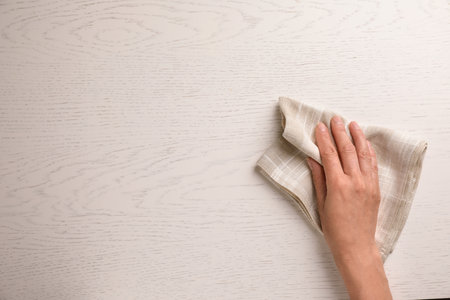 Woman wiping white wooden table with kitchen towel, top view. Space for textの写真素材