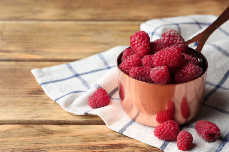 Saucepan with delicious ripe raspberries on wooden table, space for textの写真素材