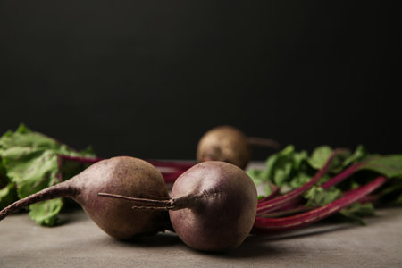 Fresh beets with leaves on gray table against black background, closeup. Space for textの写真素材