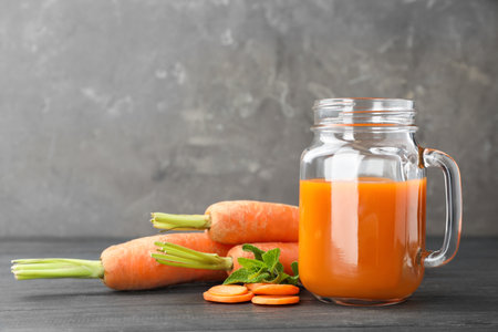 Mason jar of tasty drink and carrots on wooden table against color background, space for textの写真素材