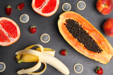 Flat lay composition with condoms and exotic fruits on black stone background. Erotic conceptの写真素材