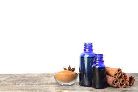 Bottles of essential oils, cinnamon sticks and powder on wooden table against white background. Space for textの写真素材