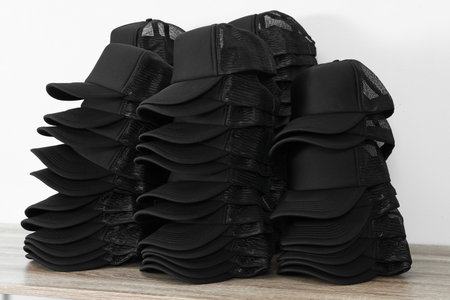 Many blank black caps on wooden table near light wall. Mock up designの写真素材