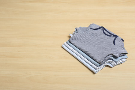 Different baby bodysuits on wooden background, space for textの写真素材