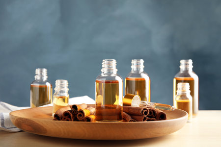 Bottles of essential oils and cinnamon sticks on table against blue backgroundの写真素材