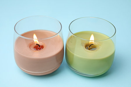 Burning wax candles in glass holders on light blue backgroundの写真素材