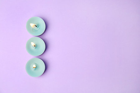 Burning wax decorative candles on purple background, flat lay. Space for textの写真素材