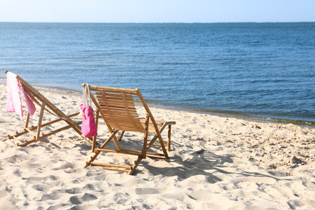 Empty wooden sunbeds and beach accessories on sandy shoreの写真素材