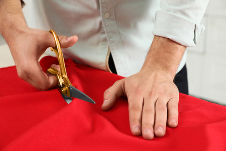 Professional tailor cutting red fabric with scissors in workshop, closeupの写真素材