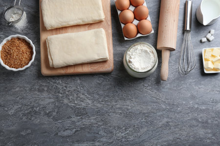 Puff pastry dough and ingredients on gray table, flat lay. Space for text