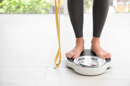 Woman with tape standing on scales indoors, space for text. overweight problemの写真素材