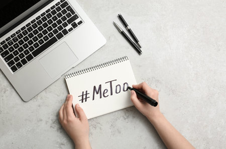 Woman writing hashtag METOO in notebook at gray table, top view. Stop sexual assaultの写真素材