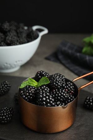 Metal saucepan with tasty blackberries on gray tableの写真素材
