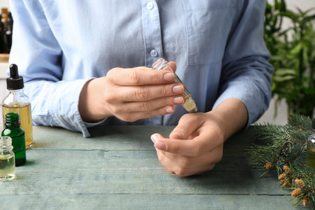 Woman applying essential oil on wrist at wooden table, closeupの写真素材