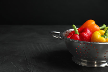 Colander with wet ripe bell peppers on gray table against black background, space for textの写真素材