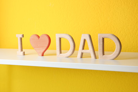 Phrase I LOVE DAD made of wooden letters on shelf near yellow wallの写真素材
