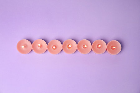 Burning wax decorative candles on purple background, flat layの写真素材