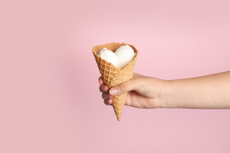 Woman holding delicious ice cream in wafer cone on pink background, closeupの写真素材