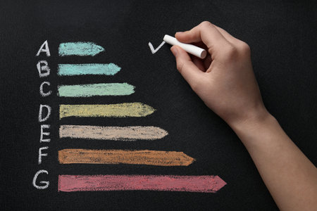 Woman checking energy efficiency level of rating chart on black background, top viewの写真素材