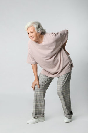 Full length portrait of senior woman having knee problems on gray backgroundの写真素材