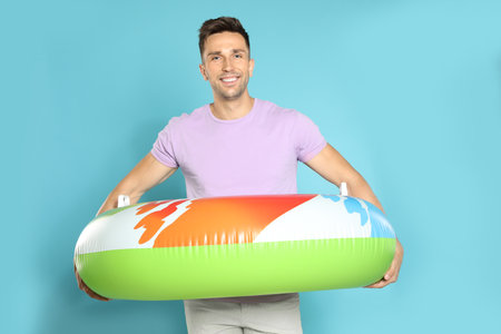 Happy young man with bright inflatable ring on blue background