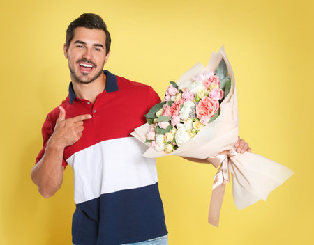 Young handsome man with beautiful flower bouquet on yellow backgroundの写真素材