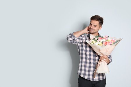 Young handsome man with beautiful flower bouquet on light background, space for textの写真素材
