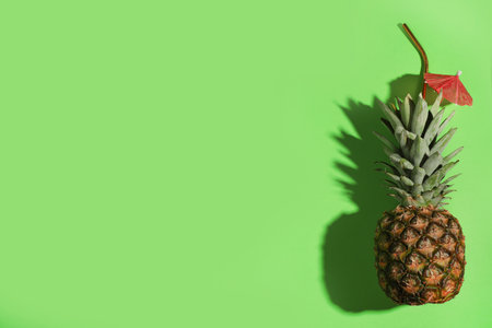 Creative composition with pineapple, straw and cocktail umbrella on green background. Space for textの写真素材