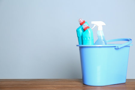 Plastic bucket with different cleaning products on table against color background. Space for textの写真素材