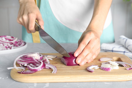Woman cutting fresh red onion on wooden board at table, closeupの写真素材
