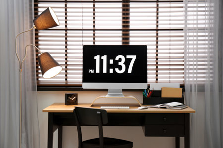 Modern PC on table near window with blinds in roomの写真素材