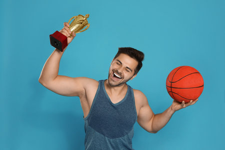 Portrait of happy young basketball player with gold trophy cup on blue backgroundの写真素材