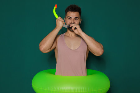 Funny young man with bright inflatable ring on dark green backgroundの写真素材