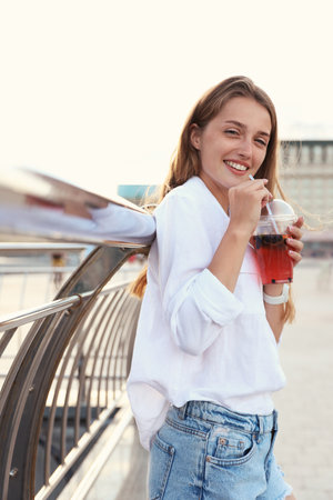 Young woman with refreshing drink on city streetの写真素材