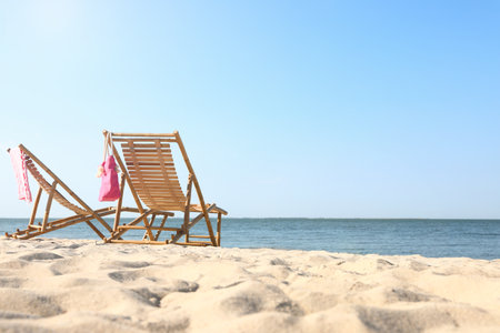 Empty wooden sunbeds and beach accessories on sandy shoreの写真素材