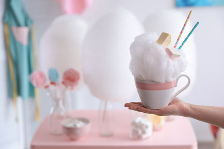 Woman holding cup with cotton candy dessert on blurred background, closeup. Space for textの写真素材