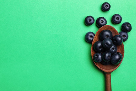 Fresh acai berries with wooden spoon on green background, flat lay. Space for textの写真素材