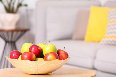 Bowl with different sweet apples on table in living room, space for textの写真素材