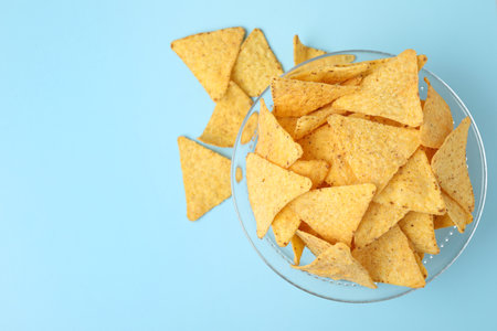 Glass bowl of tasty Mexican nachos chips on light blue background, top viewの写真素材