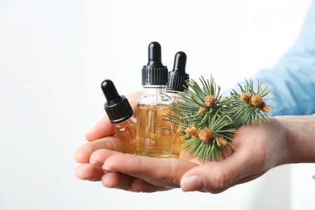 Woman holding bottles of essential oils and fir branches on white background, closeupの写真素材