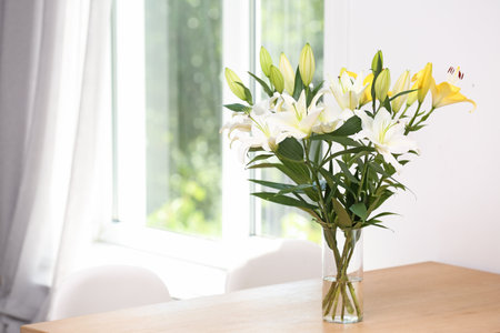 Vase with bouquet of beautiful lilies on wooden table indoors. Space for textの写真素材